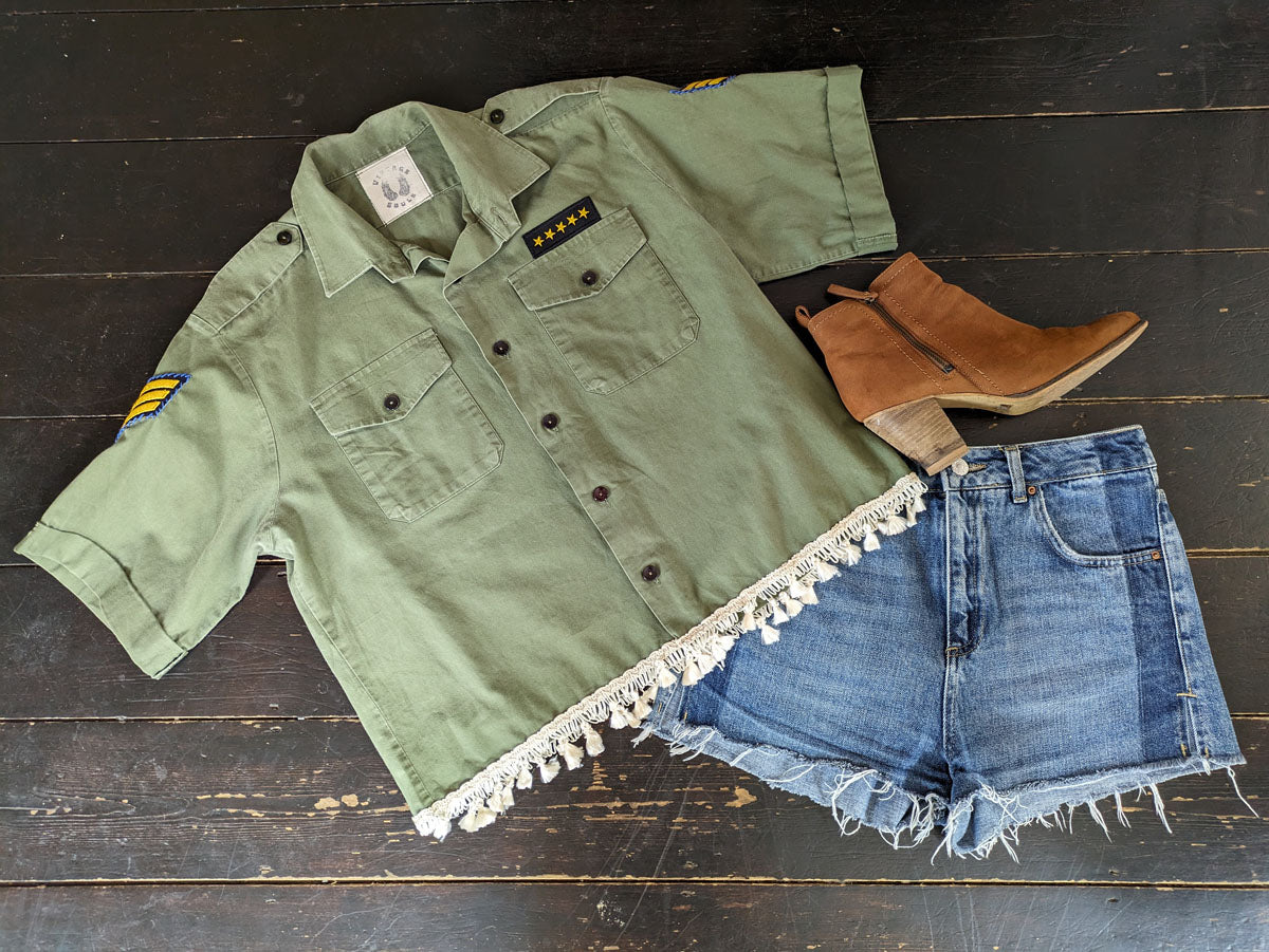 Green shirt with tassel trim, denim shorts, and brown boots on a wooden surface