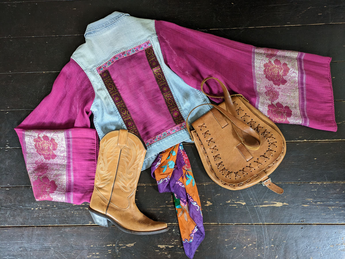 Traditional outfit with pink and blue fabric, brown boots, and a leather bag on a wooden surface