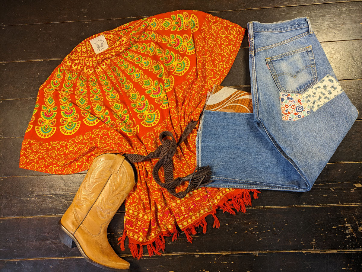 Orange patterned shawl, brown boots, and blue jeans on a wooden surface