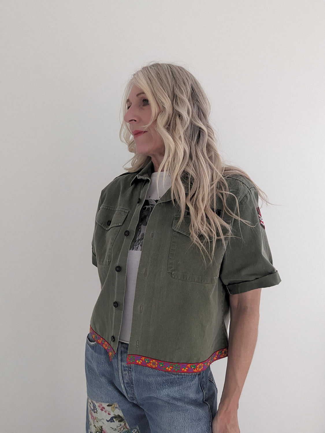 Person wearing a green jacket and blue jeans with floral patterns on a plain background