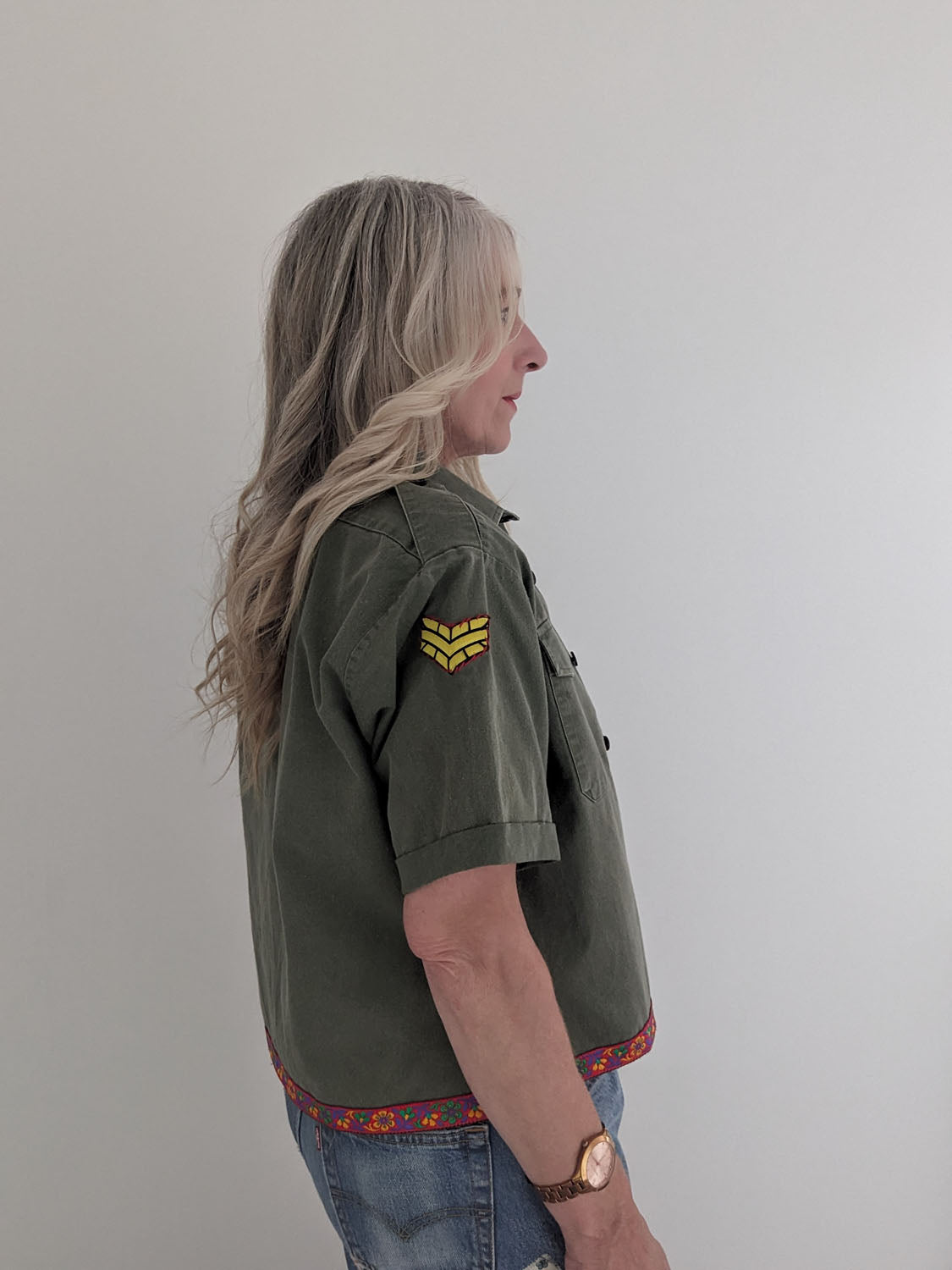 Person wearing a green shirt with a yellow patch on a plain background