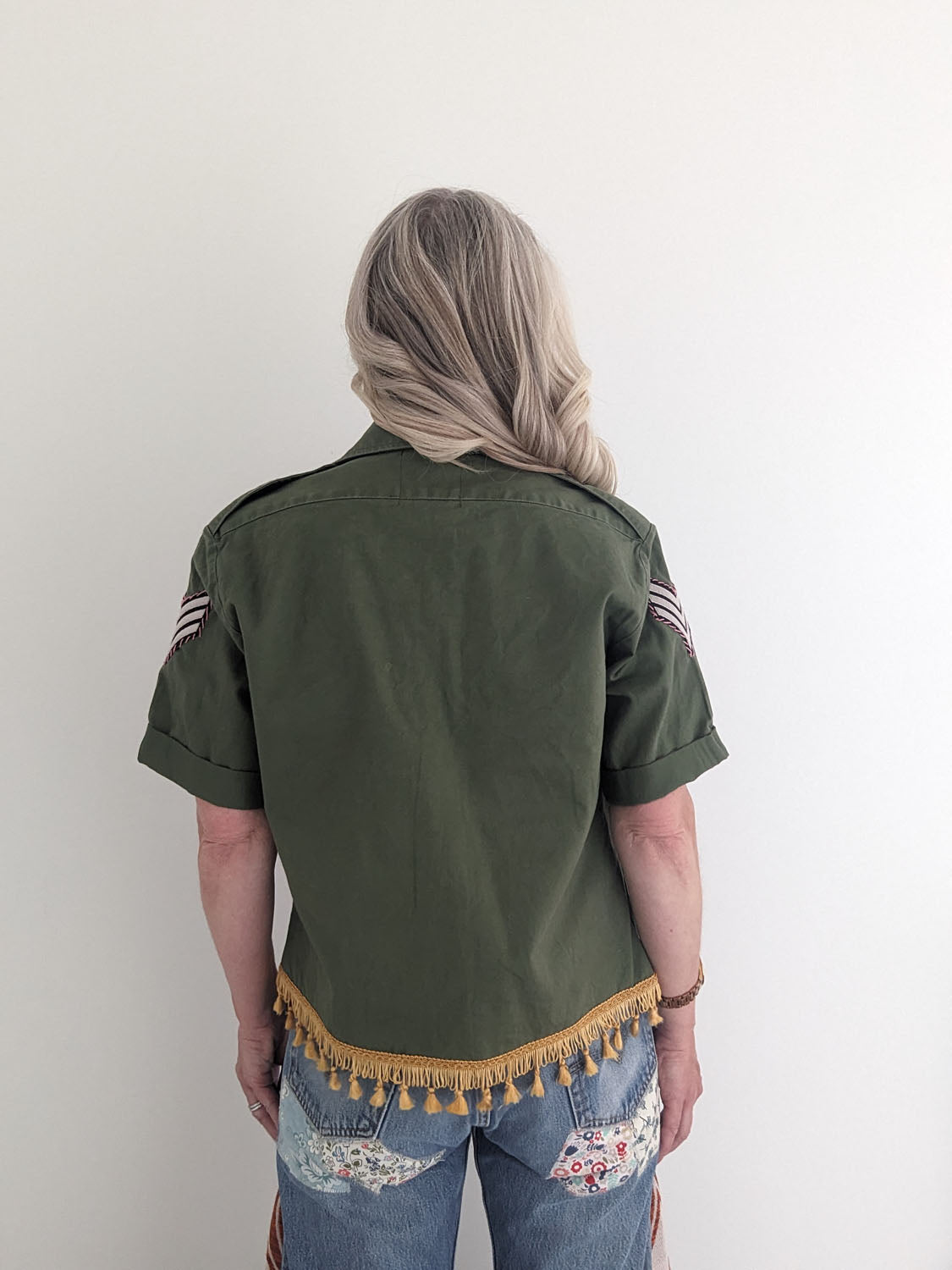 Person wearing a green jacket with tassel details on a plain background