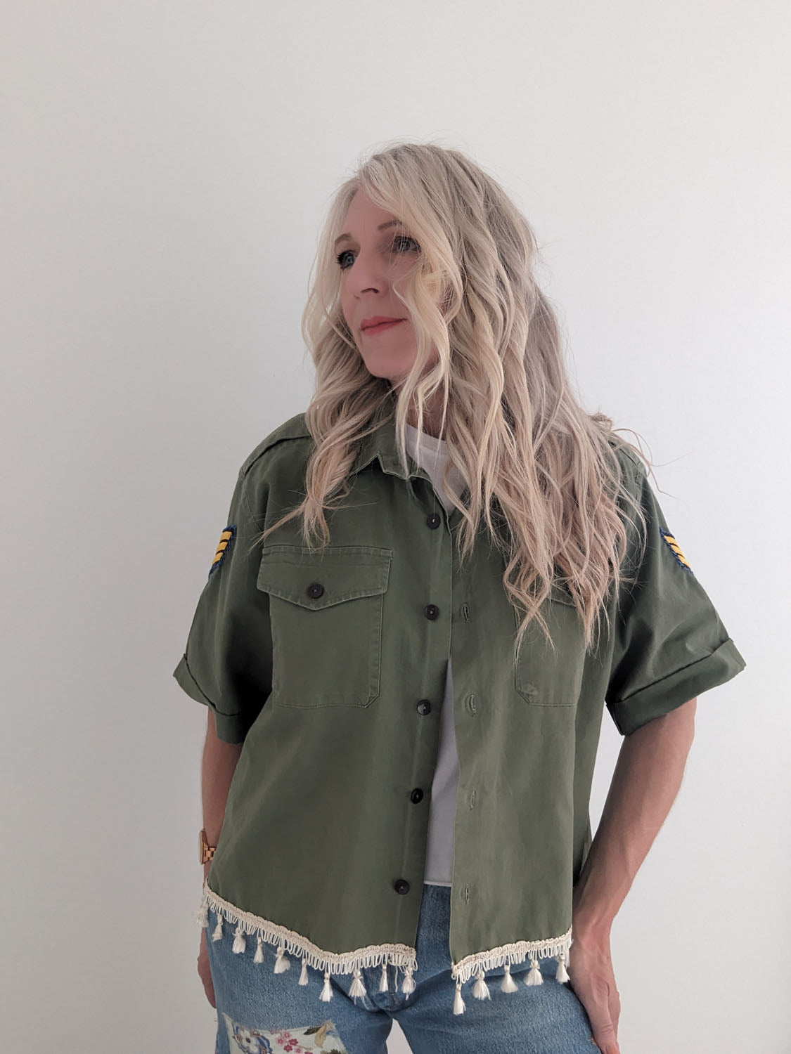 Person wearing a green military-style jacket with tassel details on a plain background