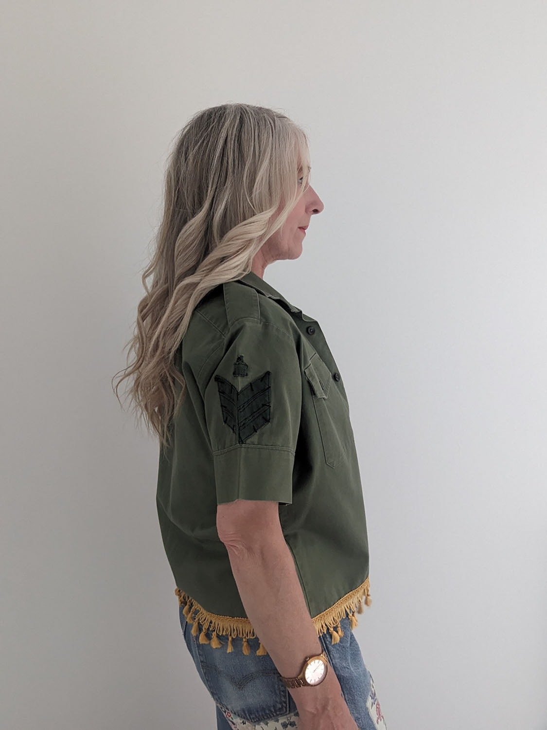 Woman wearing a green jacket with fringe details on a plain background