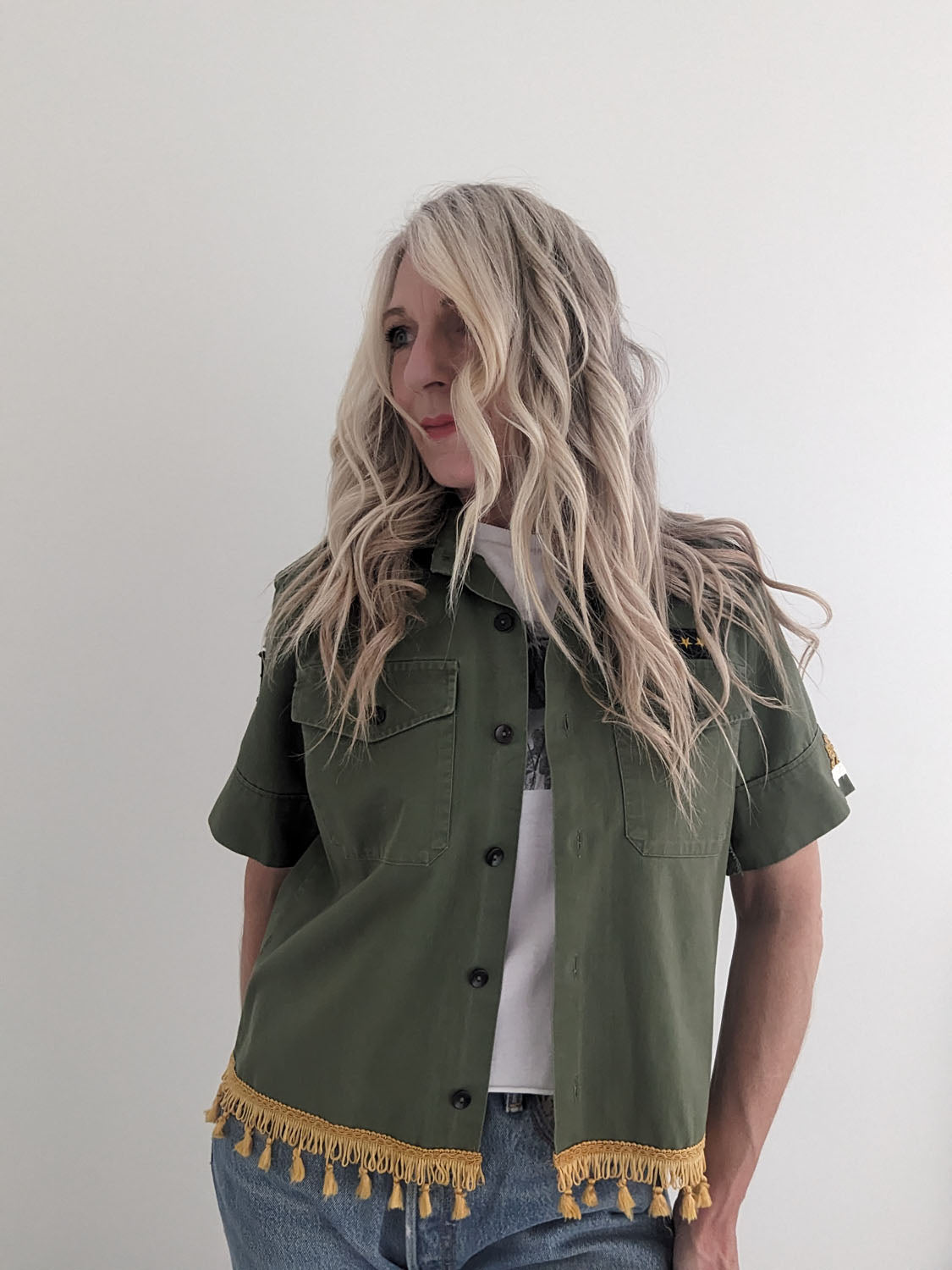 Person wearing a green jacket with yellow fringe details on a plain background