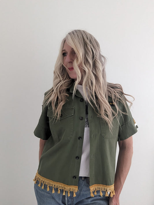 Person wearing a green jacket with yellow fringe details on a plain background