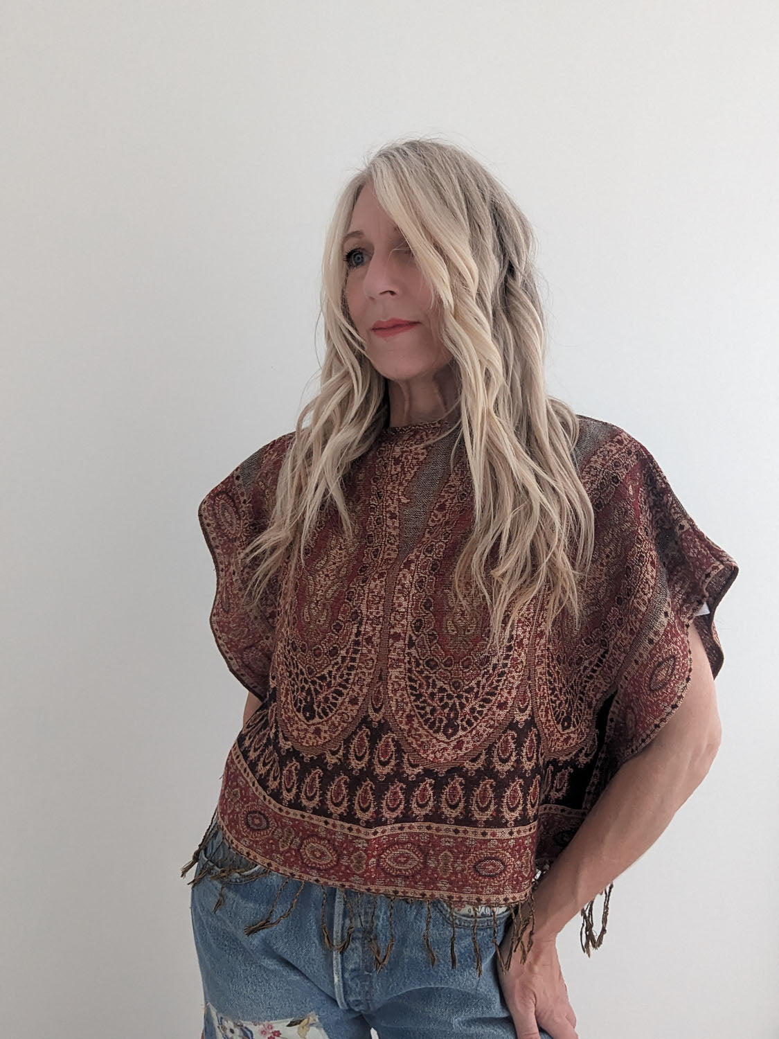 Woman wearing a patterned top and jeans against a plain background