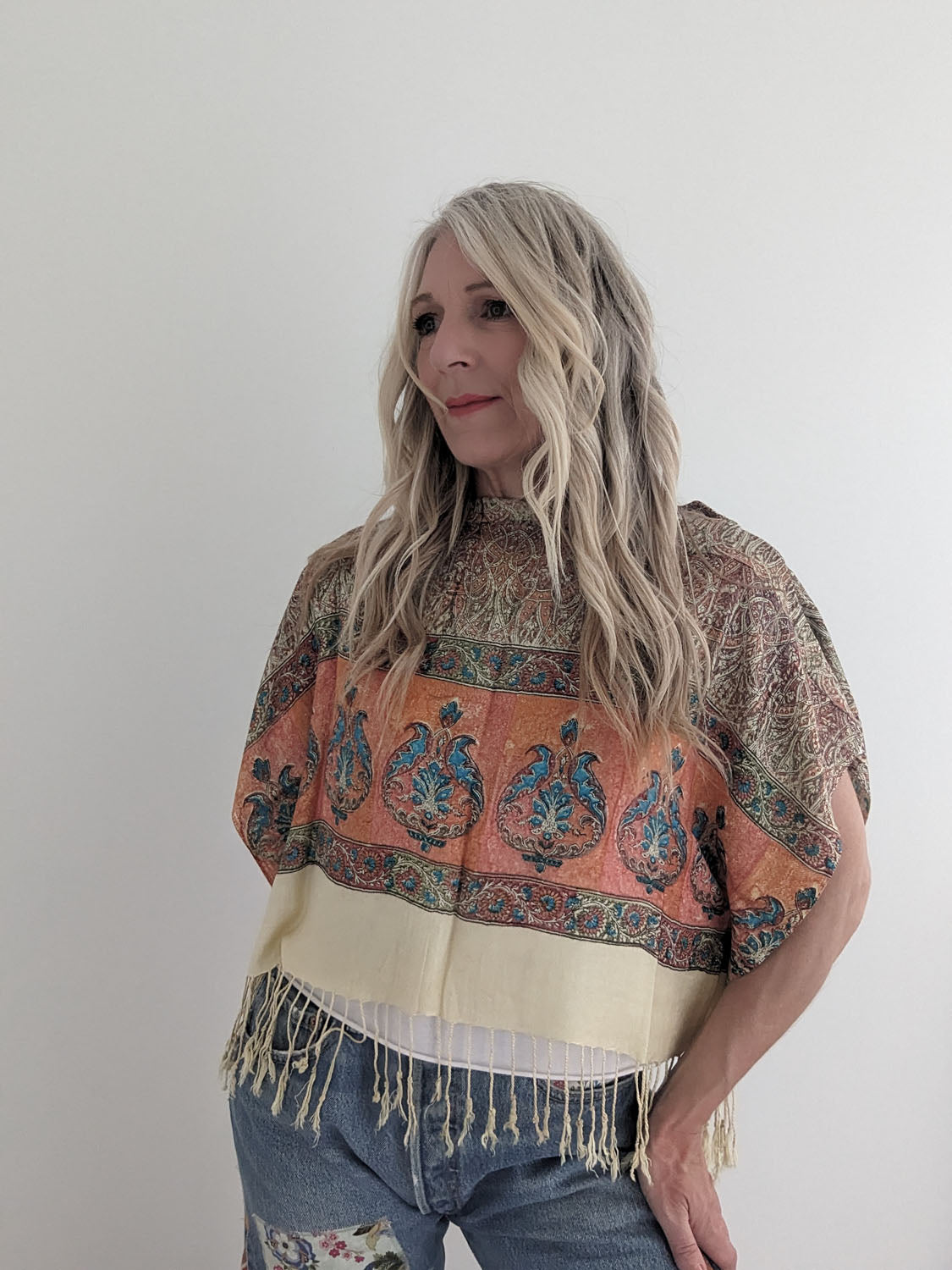 Woman wearing a patterned top with fringes on a plain background