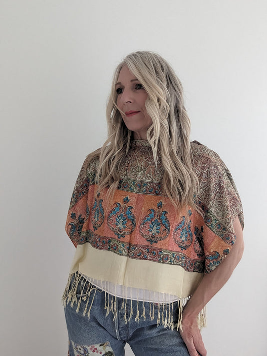 Woman wearing a patterned top with fringes on a plain background