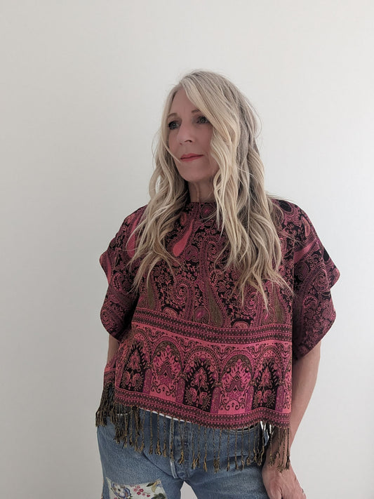 Woman wearing a patterned top with fringes against a plain background