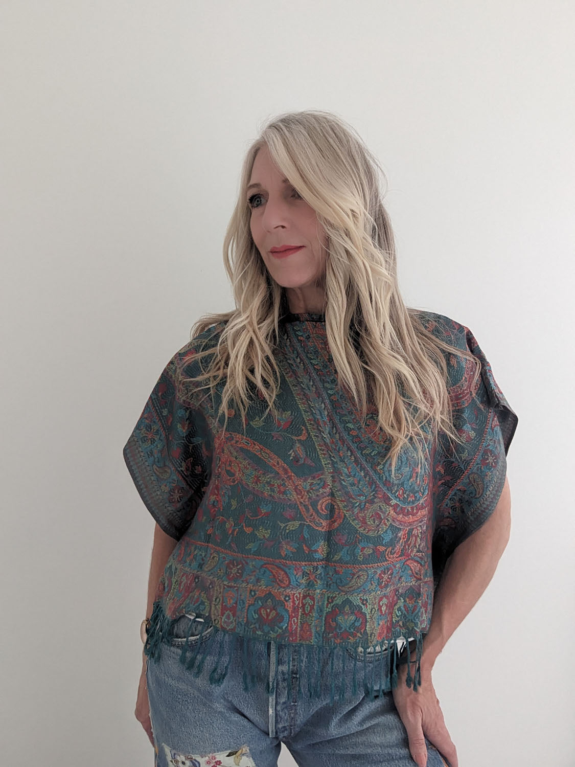 Woman wearing a patterned top and jeans against a plain background