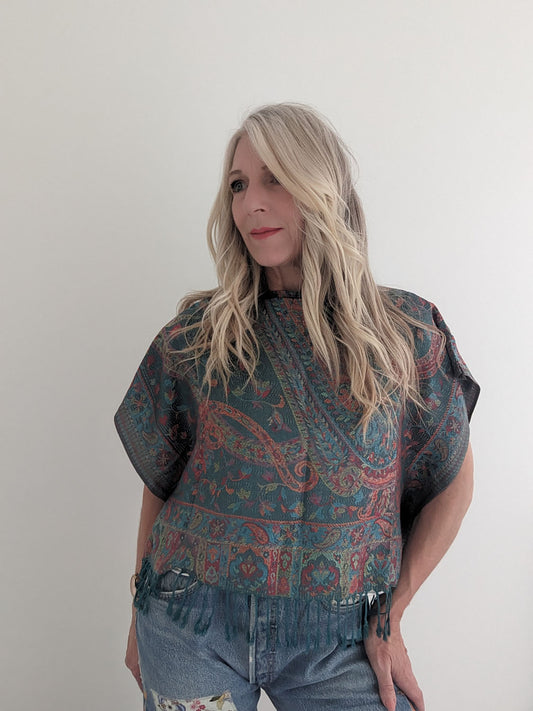 Woman wearing a patterned top and jeans against a plain background