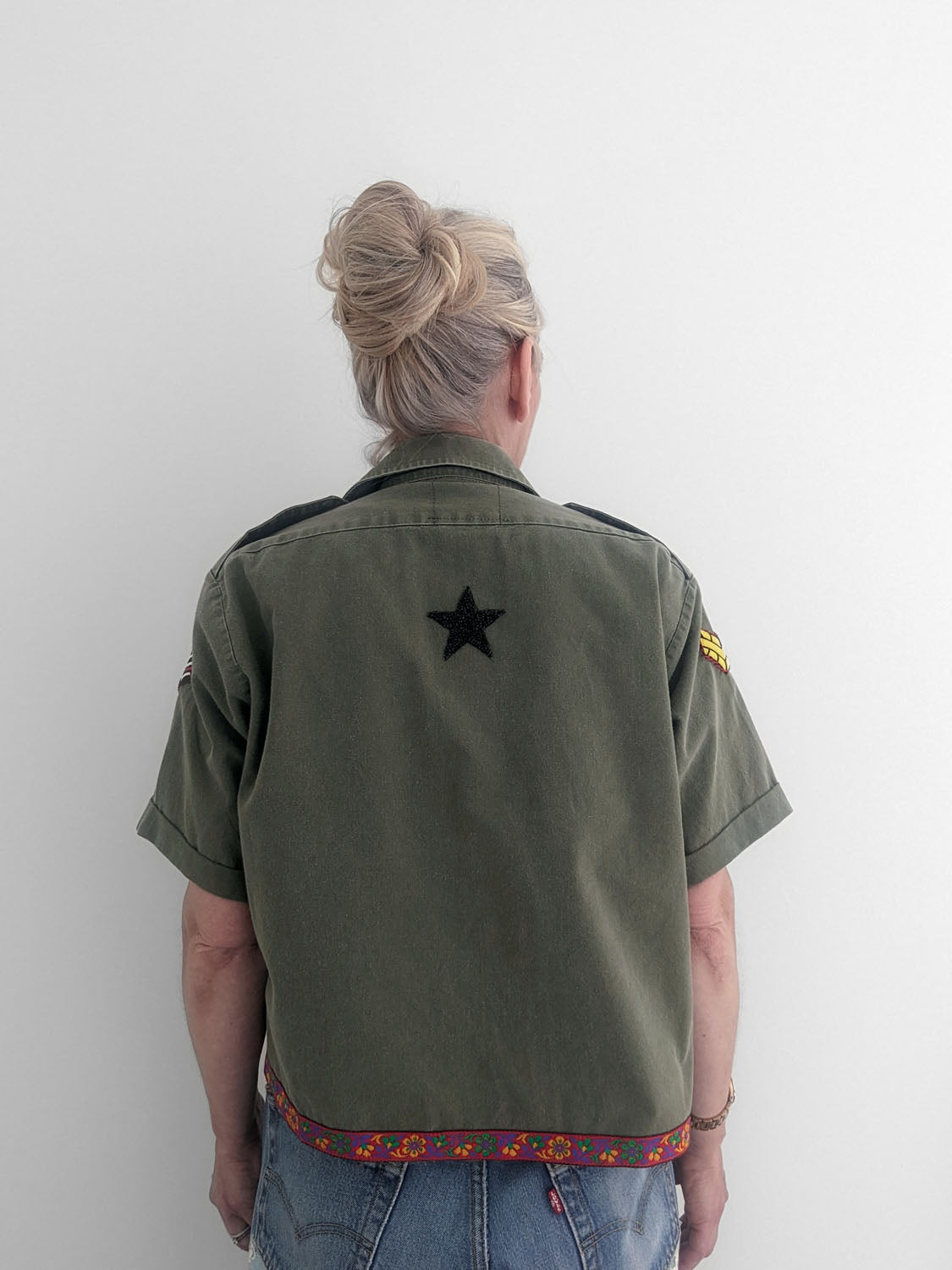Person wearing a green shirt with a star emblem on the back against a white wall