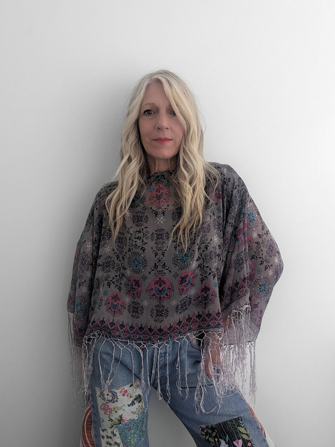Person wearing a patterned poncho and jeans against a plain background