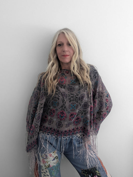 Woman wearing a patterned shawl and jeans against a plain background