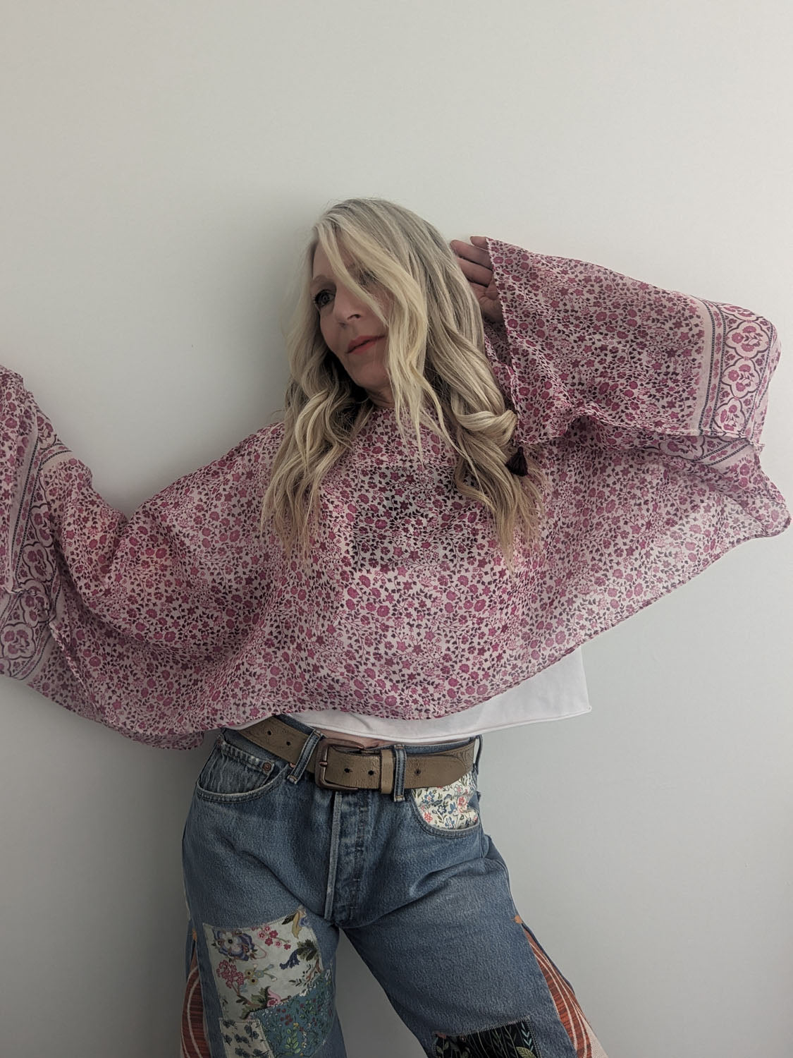 Person wearing a pink floral blouse and blue jeans against a white wall