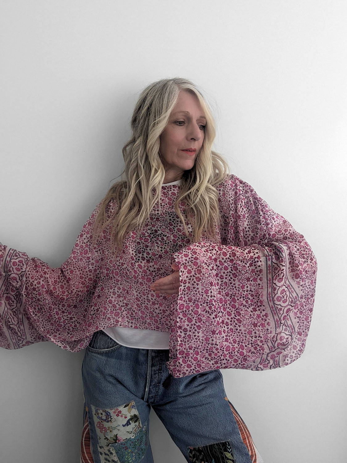Person wearing a pink patterned blouse and blue jeans against a white background