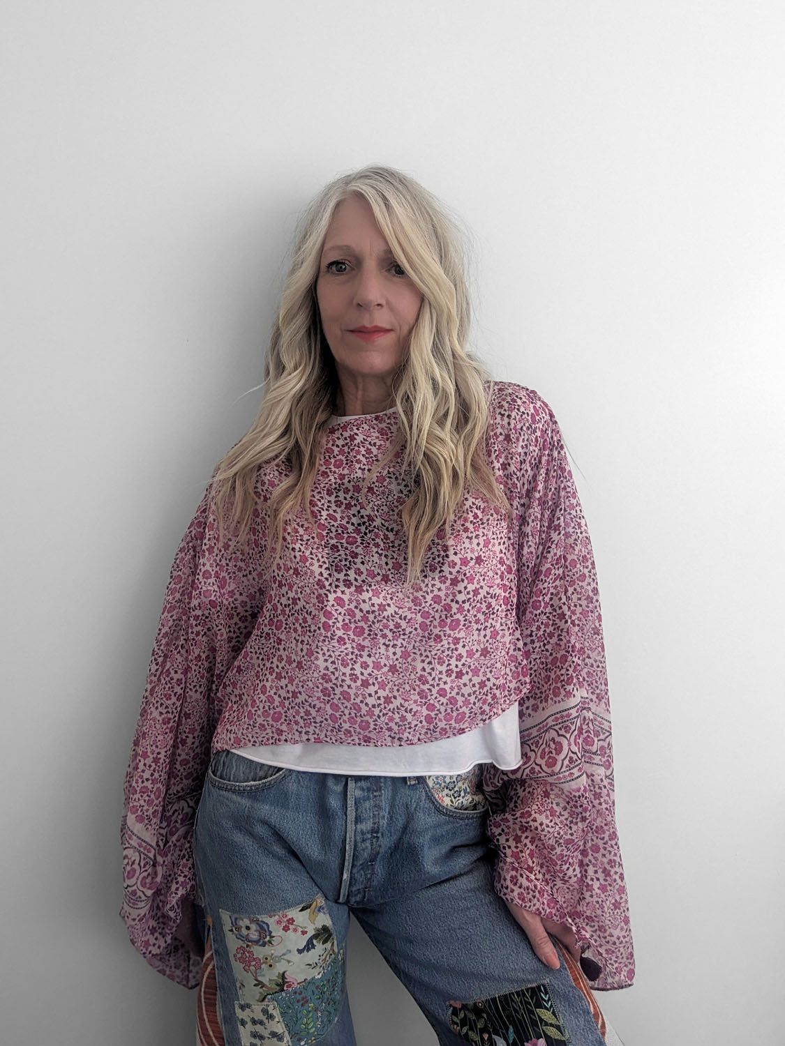 Woman wearing a patterned pink blouse and blue jeans against a plain background