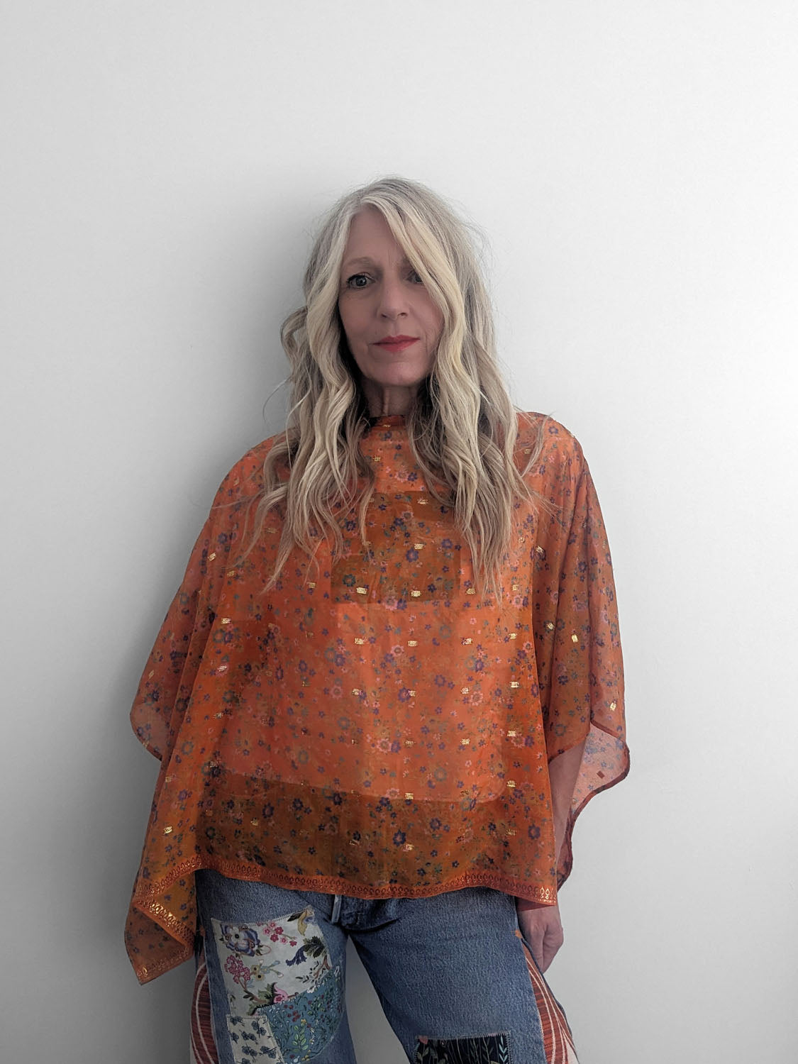 Woman wearing an orange patterned top against a plain background