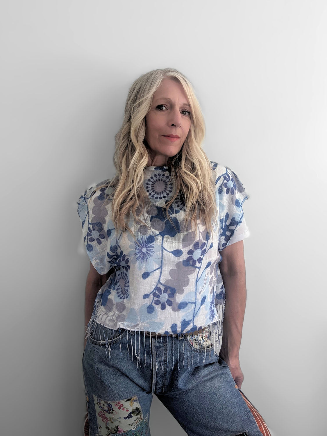 Woman wearing a floral top and jeans against a plain background