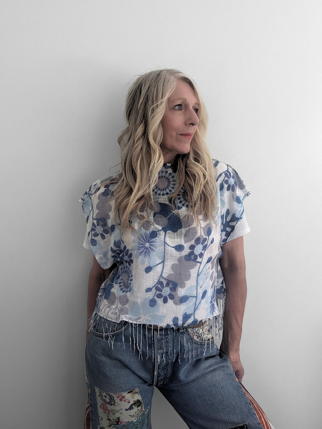 Woman wearing a floral top and jeans against a plain background