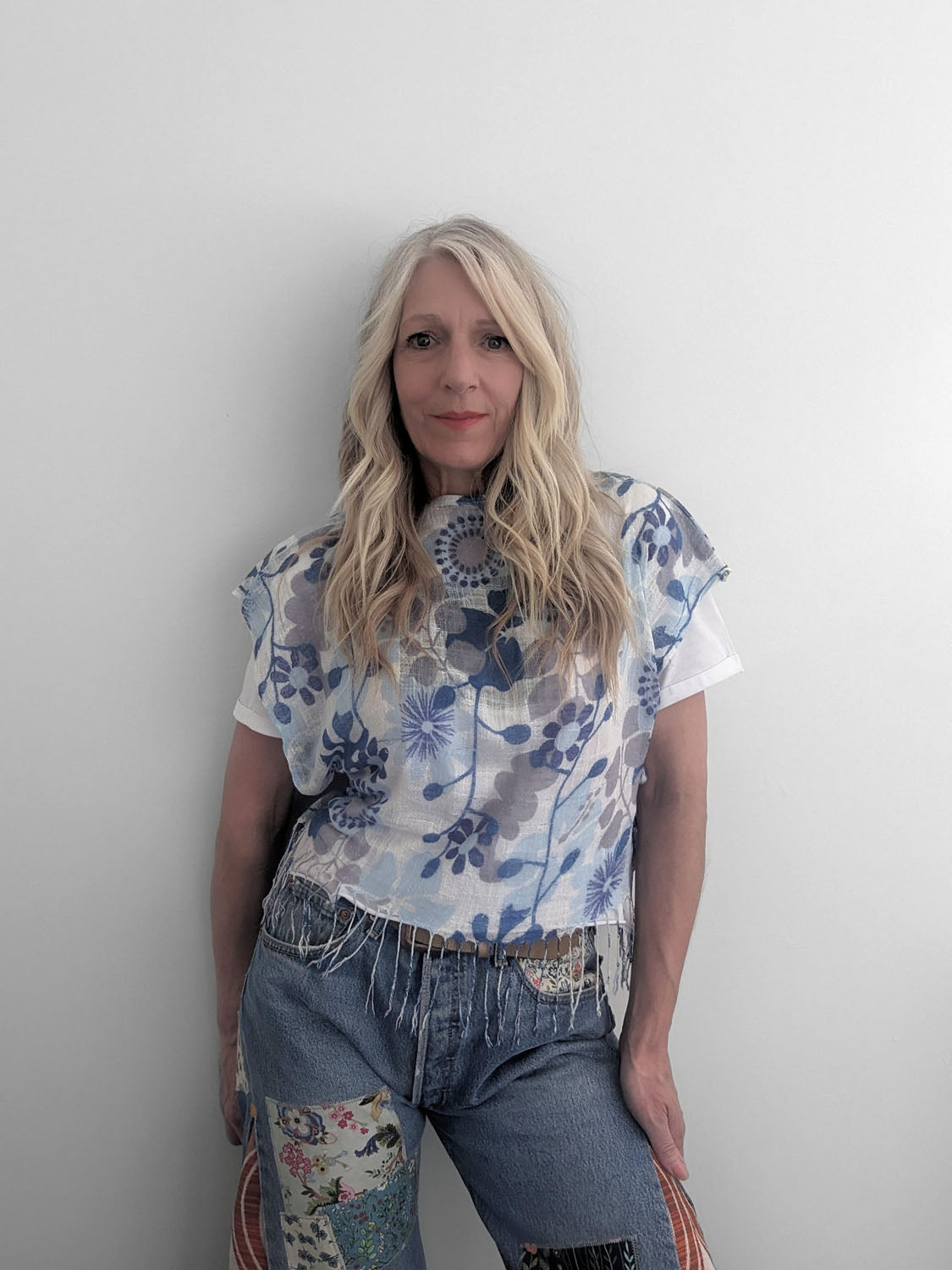 Woman wearing a floral top and jeans against a plain background