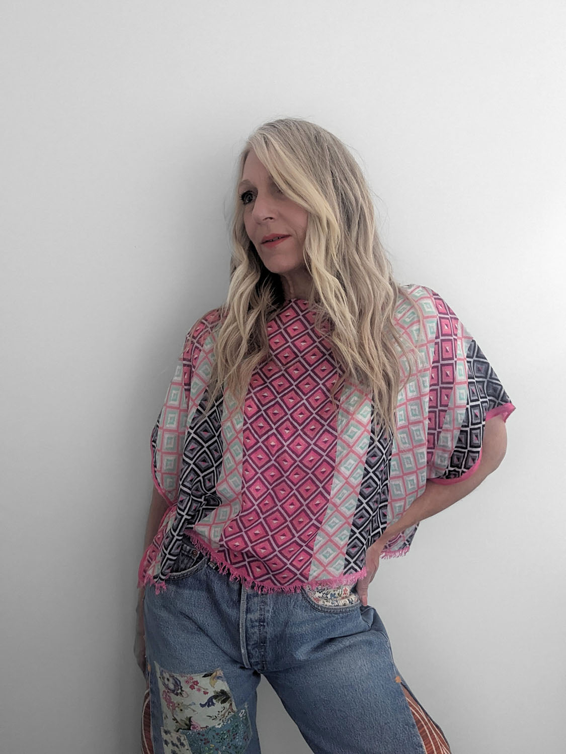 Woman wearing a patterned top and jeans against a plain background