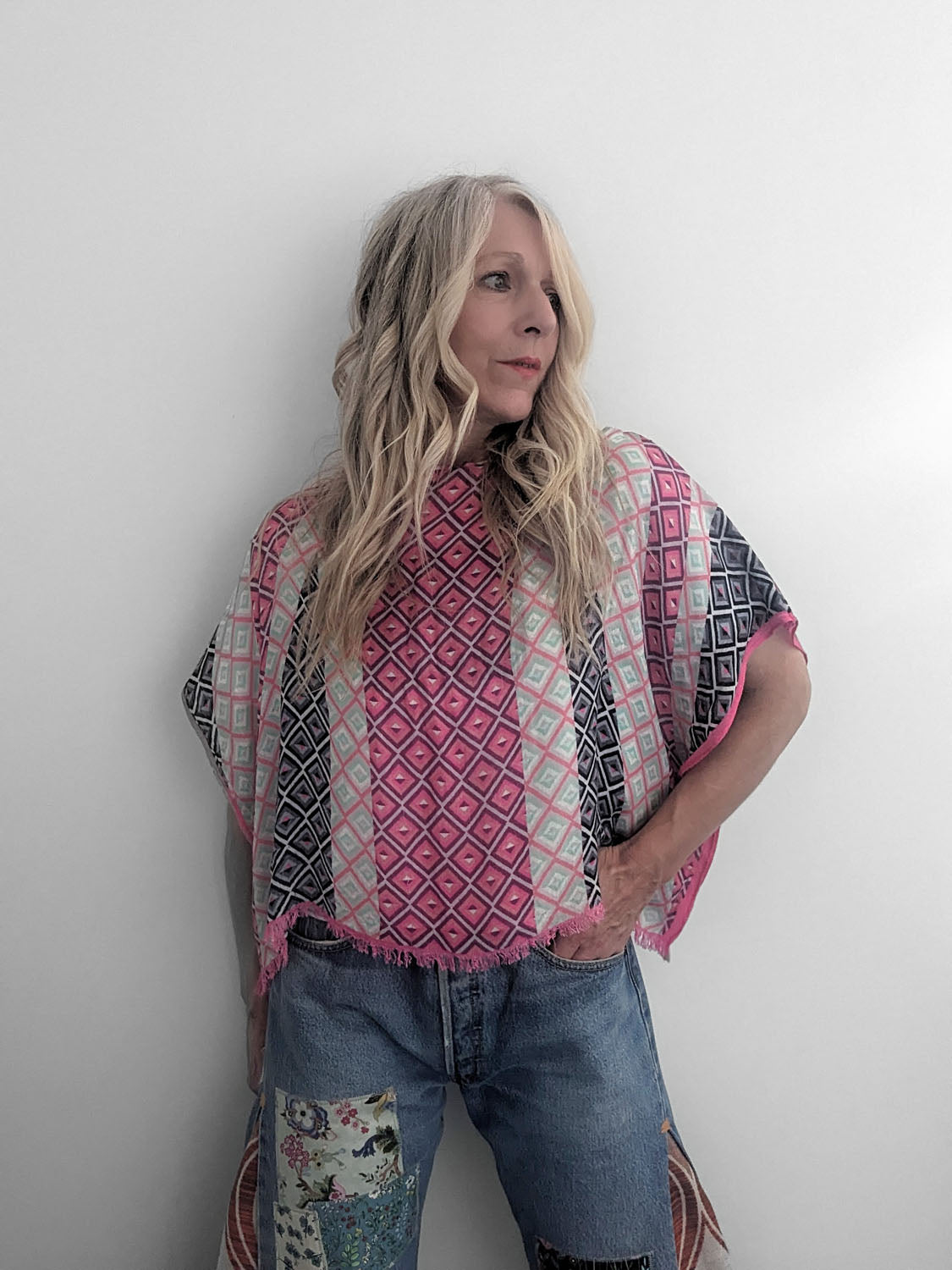 Person wearing a patterned poncho and jeans against a white background